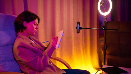 Woman holding notebook and filming coaching speech on phone. Concept of confident knowledge sharing, personal brand presence, and modern online communication.