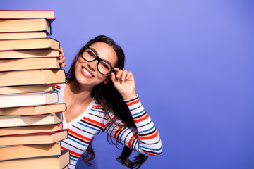 Young female student smiles while posing with a tall stack of books in a colorful striped top