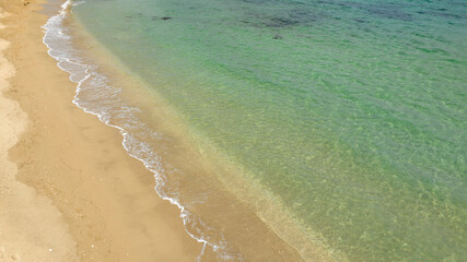 Aerial view of an empty sandy beach on a beautiful sunny summer day. The coast overlooks a dreamlike sea, turquoise, crystalline and clear.
