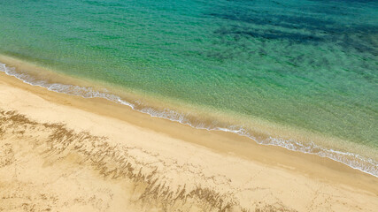 Aerial view of an empty sandy beach on a beautiful sunny summer day. The coast overlooks a dreamlike sea, turquoise, crystalline and clear.