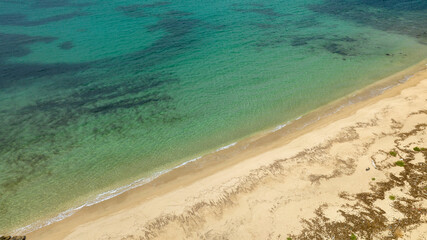 Aerial view of an empty sandy beach on a beautiful sunny summer day. The coast overlooks a dreamlike sea, turquoise, crystalline and clear.