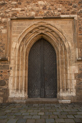 Gothic stone church entrance with pointed arch and heavy wooden doors. Historic medieval architecture detail, symmetrical facade, old European religious building exterior.