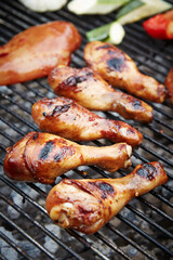 Grilling chicken drumsticks with vegetables on barbecue