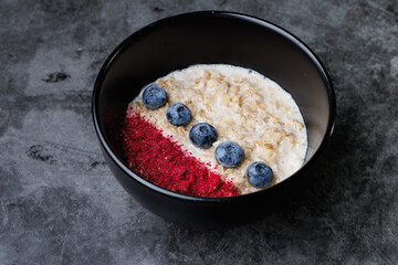 Oatmeal Bowl With Blueberries And Red Berry Powder On Dark Ceramic Plate