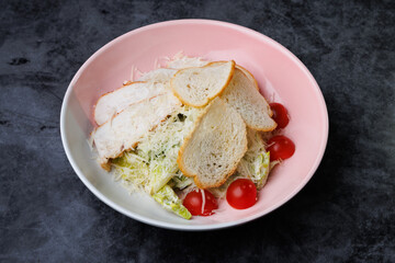 Fresh Caesar Salad With Grated Cheese, Cherry Tomatoes, and Slices of Bread on a Pink Plate