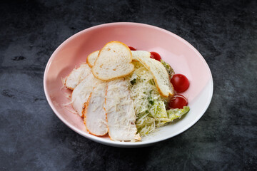 Fresh Caesar Salad With Grated Cheese, Cherry Tomatoes, and Slices of Bread on a Pink Plate