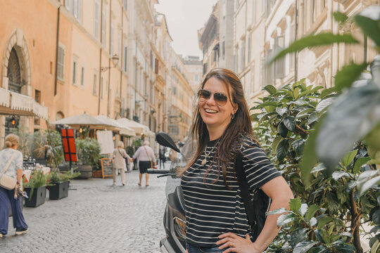 Retrato estilo de vida de turista mujer sonriendo en una pintoresca calle peatonal de Roma, Italia. Arquitectura tradicional de edificios ocres y suelo de adoquines (sampietrini).