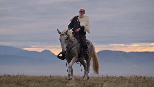Elderly Viking warrior in fur cloak riding gray horse across open field at sunrise, mountains and distant cross behind him, moody cinematic Norse atmosphere cinematic slow motion 