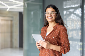 Young happy indian business woman wearing glasses and a brown polka dot shirt smiling while holding...