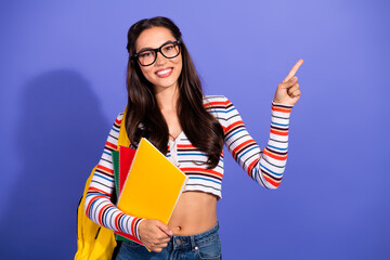 Young female student with colorful notebooks points toward the top against a violet studio background showing style confidence and school life