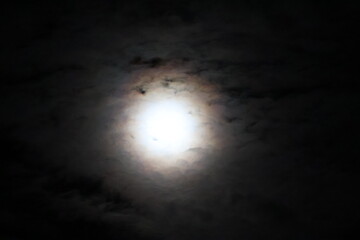A bright full moon glows in the dark night sky, casting soft light across the darkness and creating...