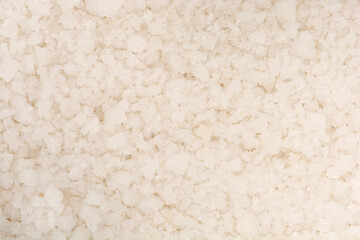 A close-up, high-angle texture shot fills the frame with coarse, irregular white and off-white granules of natural sea salt