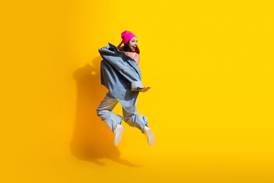 Young woman leaps in denim streetwear against bright yellow background capturing joyful fashion moment