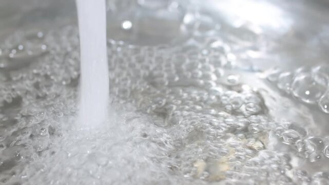 Water flows from a faucet to the sink. Air bubbles. In slow motion.