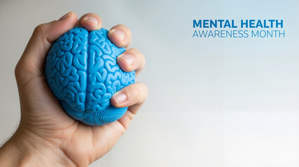 Hand holding blue brain-shaped stress ball during Mental Health Awareness Month with copy space