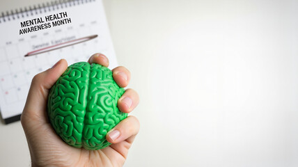 Hand holding green brain-shaped stress ball with calendar showing Mental Health Awareness Month, copy space