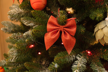 Close up of Christmas tree decorated with shiny red bow and colorful ornaments. 