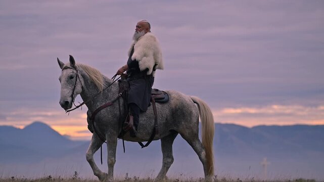 Elderly Viking warrior in fur cloak riding gray horse across open field at sunrise, mountains and distant cross behind him, moody cinematic Norse atmosphere cinematic slow motion 