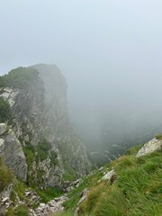 Steep rocky mountain cliff disappearing into dense fog. Rocky mountain cliff in thick fog. 