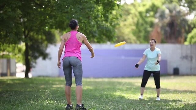 Two women enjoying throwing and catching a frisbee in the park