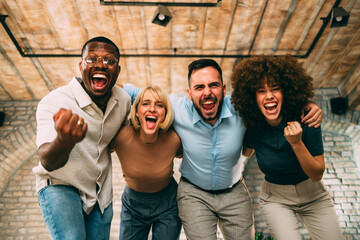 Excited diverse business team cheers loudly and hugs, celebrating a great success or achievement in the office
