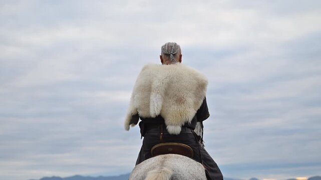 Elderly Viking warrior in fur cloak riding gray horse across open field at sunrise, mountains and distant cross behind him, moody cinematic Norse atmosphere cinematic slow motion 