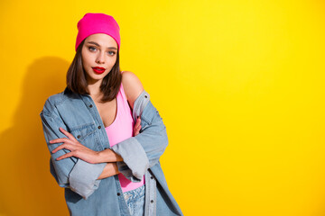 Young female fashion model in denim jacket pink top and beanie posing against bright yellow background for streetwear style and glamour advertising
