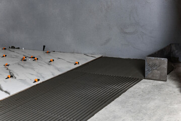 Applying tile glue to the floor using a tiling comb.