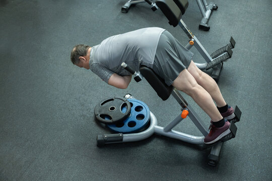 Adult man performs back extension on bench in gym, strengthening lower back muscles and core stability during workout.