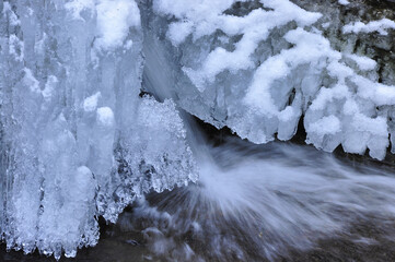 Rezerwat przyrody "Wąwóz Myśliborski" w zimowej scenerii. Zimowe formacje lodowe wzdłuż ośnieżonego brzegu rzeki z soplami i płynącą wodą. © Pol Badger