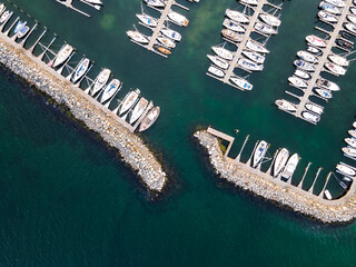 Aerial view of white boats nestled closely in the marina's teal waters, bisected by stone jetties, creating a striking contrast of textures and tones., Moss, Norway.