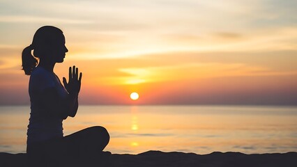 Silhouette of a woman meditating in a serene yoga pose on a sandy beach at sunset with the ocean and golden sky in the background