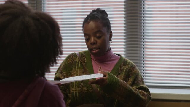 Rack focus of black woman holding failed test of teenage daughter while having tense conversation in school office