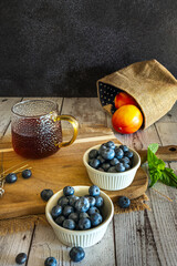 Small white porcelain bowls arranged in a row showcase variations in the quantity and arrangement of blueberries on the rustic white wooden surface