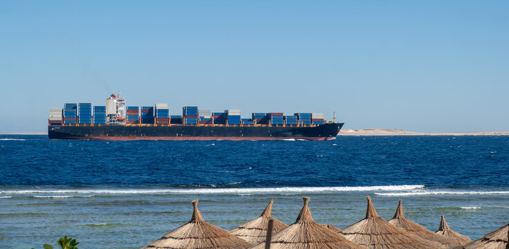 A Large Cargo Ship Navigates Calm Waters Near a Sandy Shoreline on a Clear Sunny Day