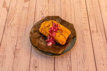 Colombian tamale filled with chicken, chickpeas, carrots, and capers, presented in a bijao leaf wrapper