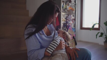 Mother cradling breastfeeding toddler in soft light while seated on stairs creating serene nurturing moment blending tenderness maternal comfort and quiet presence within peaceful home environment