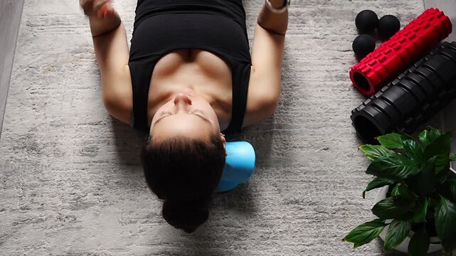 Young woman lies on the floor using a blue cervical traction device to stretch the neck. Home therapy for neck pain, muscle tension and spine decompression.