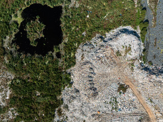 Aerial view showing a stark contrast between a natural wetland with a dark pond and a nearby landfill area.