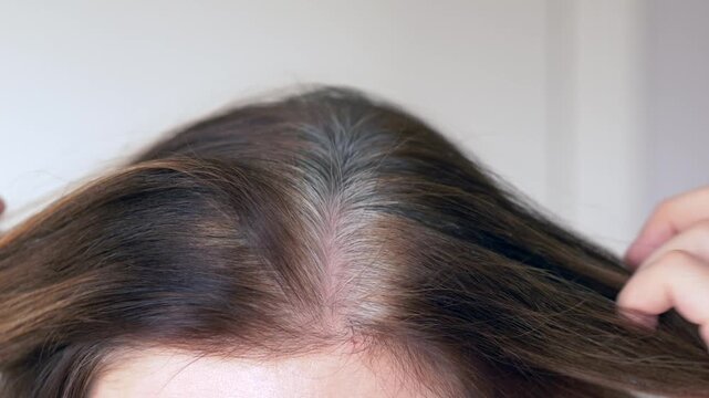 Close view of gray hair at the scalp as woman reveals gray hairs along roots. Clip shows natural color transition, authentic texture and aging signs ideal for beauty brands. Brunette with gray roots.