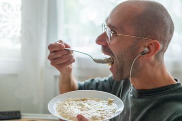 Young man eating oatmeal while working computer desk, multitasking breakfast with healthy food during busy office routine, combining nutrition and productivity lifestyle, professional modern lifestyle