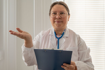 experienced female woman doctor or nurse in white lab coat with stethoscope and blue clipboard,...