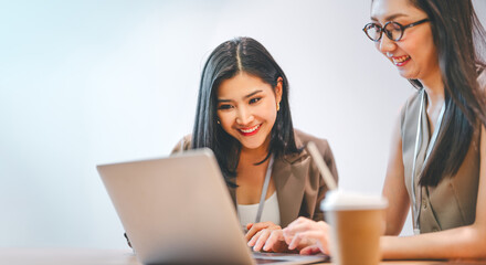Two business asian woman talking teamwork working on laptop at indoors cafe