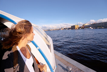 Fototapeta premium Young woman on a deck of a boat observs a cityscape coastline. Petersburg, Russia.