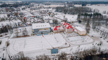 Obraz premium Rujiena, Latvia - November 27, 2025: Aerial view of snowy landscape featuring sports complex and residential area in winter season with copy space
