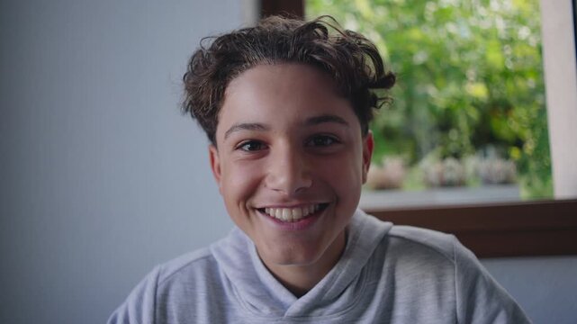 Teenage boy smiling brightly at table with warm friendly expression creating positive cheerful moment filled with openness youthfulness and relaxed comfort in natural home setting
