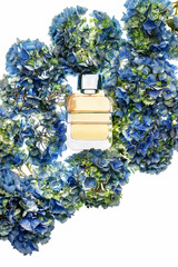 A clear bottle of fragrance is placed in the center, surrounded by blue hydrangea flowers. The setting has a bright white background, highlighting the colors and shapes.