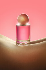 A bottle of perfume stands on a smooth curve of skin against a bright pink background. The scene is set in a studio with focused lighting highlighting the bottle's shape.