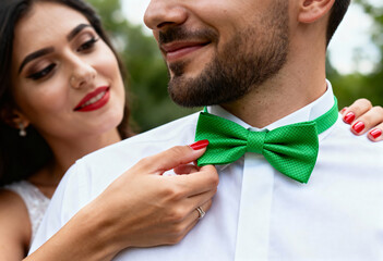 A woman adjusts her partner's vibrant green bow tie in a close-up shot. A loving couple preparing for a wedding or formal event outdoors