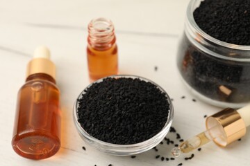 Black cumin seeds and bottles of essential oil on light wooden table, closeup